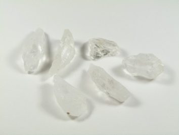 Sześć przezroczystych kryształów kwarcu leży na białym tle.