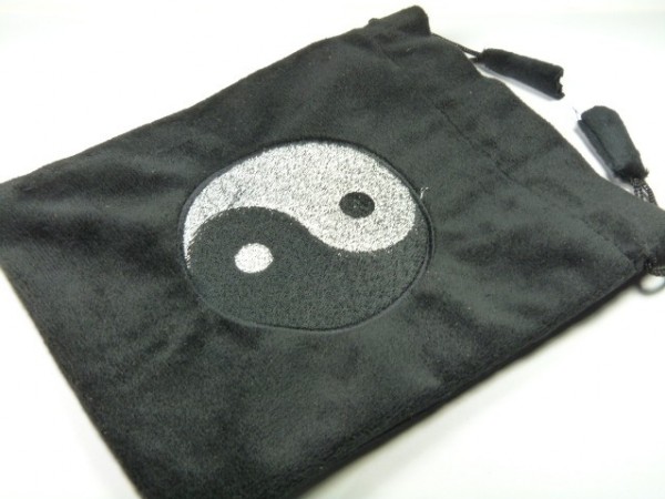 Czarny woreczek z symbolem yin-yang na środku, leżący na białym tle.