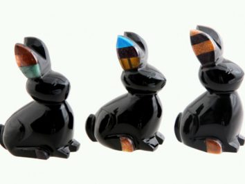 Trzy czarne figurki królików z kolorowymi uszami ustawione obok siebie na jasnym tle.