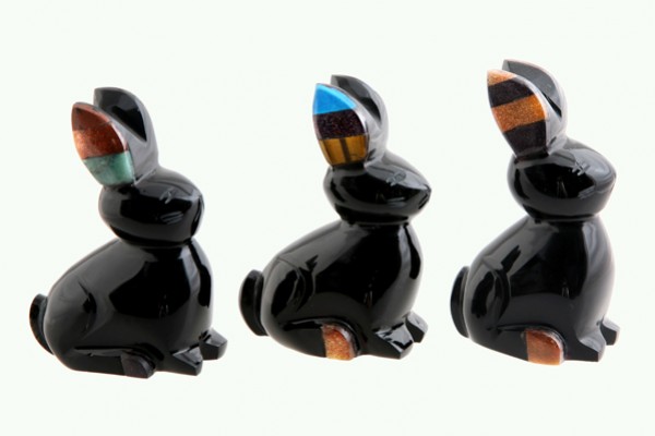 Trzy czarne figurki królików z kolorowymi uszami ustawione obok siebie na jasnym tle.