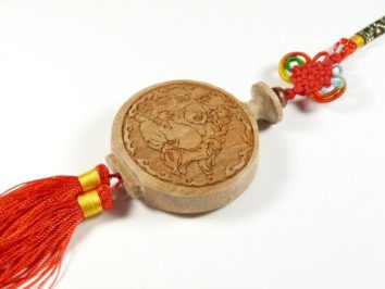 Drewniany amulet z chińskim grawerunkiem i czerwoną ozdobną frędzlą.