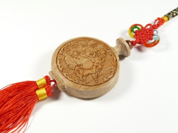 Drewniany amulet z chińskim grawerunkiem i czerwoną ozdobną frędzlą.