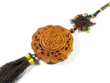 Chiński amulet z brązu z ozdobnym wzorem i frędzlem, leży na białym tle.