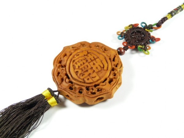 Chiński amulet z brązu z ozdobnym wzorem i frędzlem, leży na białym tle.