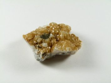 Syderyt - kamień naturalny, surowy, nieszlifowany. Kawałek błyszczącego, żółtobrązowego minerału na białym tle.