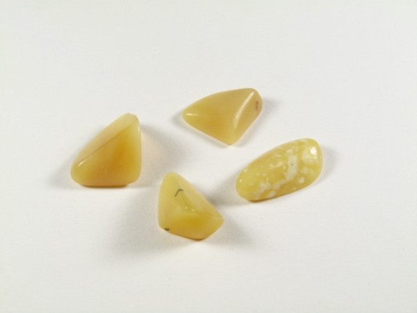 Opal miodowy - kamień gładzony, polerowany, szlifowany i bębnowany w formie otoczaka. Cztery żółte, gładko oszlifowane kamienie na białym tle.