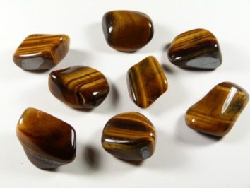 Osiem wypolerowanych kamieni tygrysiego oka leży na białej powierzchni.
