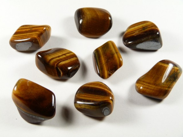 Osiem wypolerowanych kamieni tygrysiego oka leży na białej powierzchni.