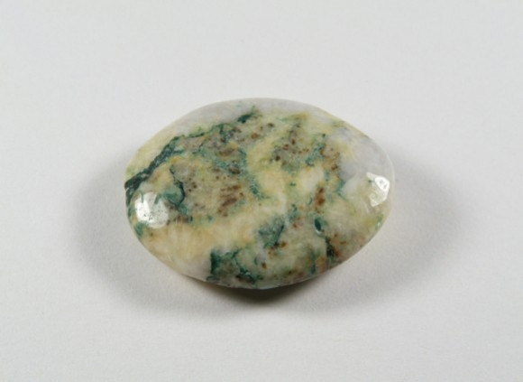 Maripozyt - kamień gładzony, polerowany, szlifowany . Wypolerowany kamień o zielono-białych wzorach leży na jasnym tle.