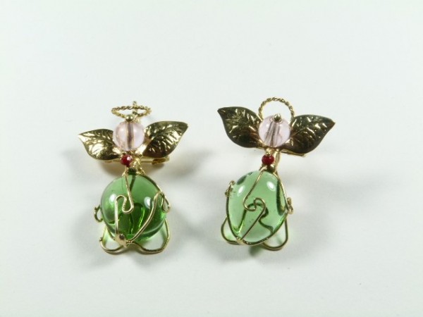 Dwie broszki w kształcie aniołków z zielonymi koralikami i złotymi skrzydłami na białym tle.