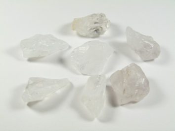 Siedem przezroczystych kryształów kwarcu ułożonych na białym tle.