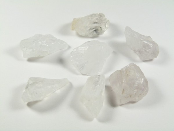 Siedem przezroczystych kryształów kwarcu ułożonych na białym tle.