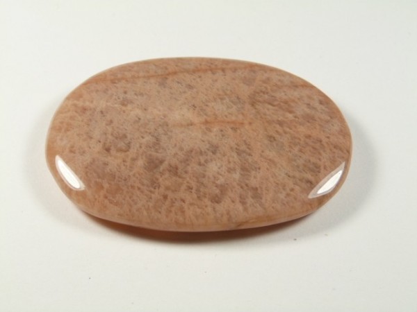 Kamień księżycowy - kamień gładzony, polerowany, szlifowany. Gładki, owalny kamień w odcieniu jasnego brązu leży na białym tle.