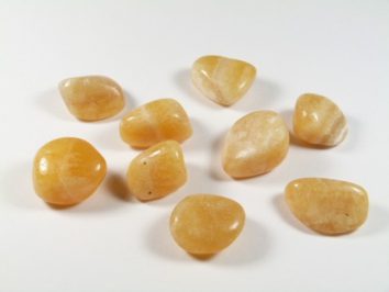 Kalcyt złoty/ kalcyt złocisty - kamień gładzony, polerowany, szlifowany i bębnowany w formie otoczaka. Dziewięć gładkich, pomarańczowych kamieni leży na białym tle.