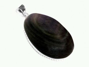 Owalny wisior z ciemnym kamieniem oprawionym w srebro, na jasnym tle.
