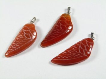 Trzy wisiorki w kształcie skrzydeł z czerwonego kamienia, ułożone na białym tle.