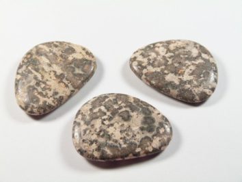 Jaspis skóra leoparda szlifowany płaski kamień. Trzy gładkie, owalne kamienie o marmurkowym wzorze leżą na białym tle.