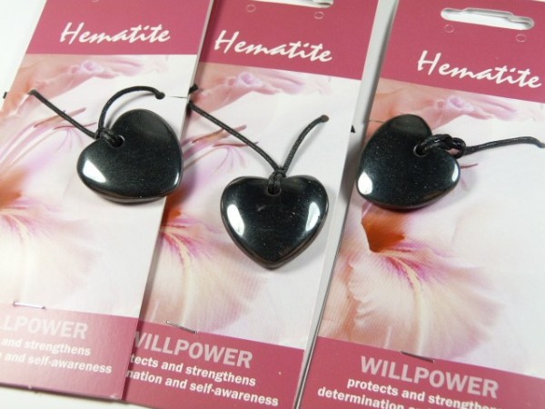 Trzy czarne wisiorki z hematytu w kształcie serca na kartonikach z napisem „Hematite”.