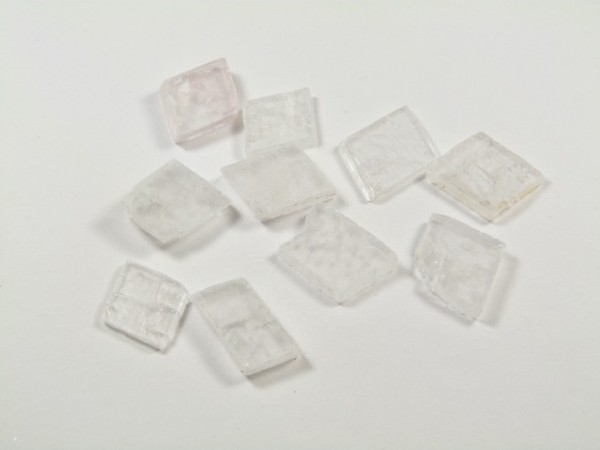 Spar islandzki - kamień naturalny, surowy, nieszlifowany. Kilka przezroczystych, kwadratowych kryształków leży na białym tle.