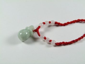 Jasnozielony jadeitowy wisiorek na czerwonym sznurku z białymi koralikami, na białym tle.
