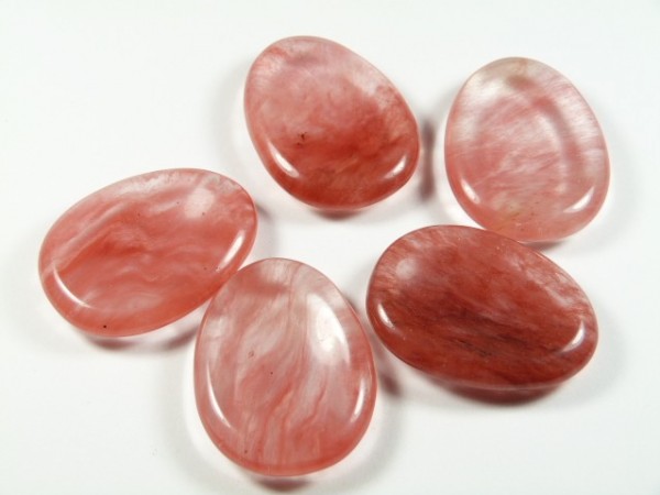 Kwarc wiśniowy szlifowany - płaski kamień. Pięć gładkich, różowych kamieni leży na białym tle.