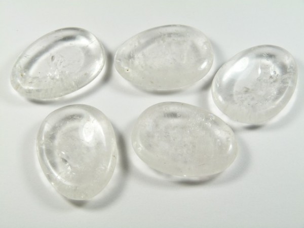 Kryształ górski szlifowany - płaski kamień. Pięć przezroczystych, gładkich kamieni leży na białym tle.