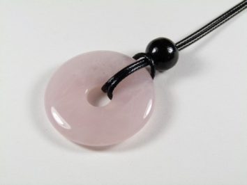 Różowy, okrągły wisiorek z kamienia na czarnym sznurku z koralikiem.