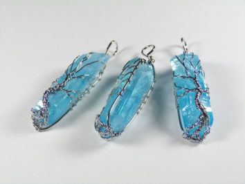 Trzy błękitne kryształy owinięte srebrnym drucikiem, tworzące wisior.