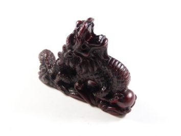 Figurka ciemnoczerwonego smoka chińskiego ustawiona na białym tle.