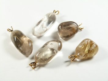 Pięć polerowanych zawieszek z kwarcu rutylowego z metalowymi uchwytami na białym tle.