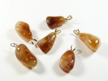 Sześć kamieni bursztynu z metalowymi zawieszkami, ułożonych na białym tle.