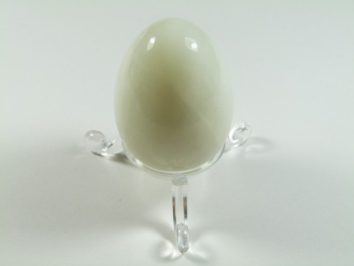 Jajko jadeit szlifowany. Białe, gładkie jajko z kamienia ustawione na przezroczystej podstawce.
