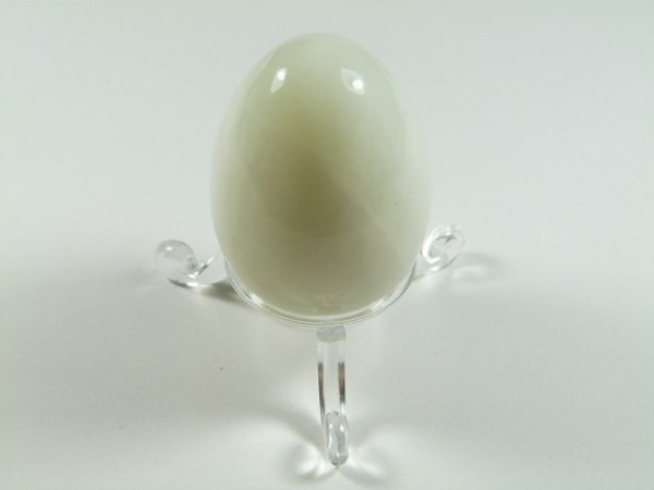 Jajko jadeit szlifowany. Białe, gładkie jajko z kamienia ustawione na przezroczystej podstawce.