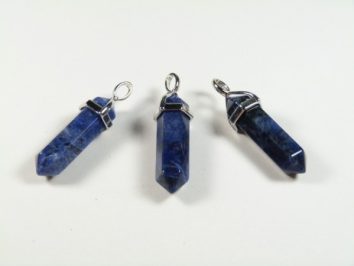 Trzy niebieskie, sześciokątne wisiorki z kamieni na białym tle.