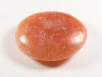 Gładki, pomarańczowy kamień leży na białym tle.