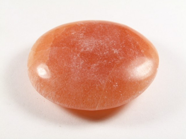 Gładki, pomarańczowy kamień leży na białym tle.