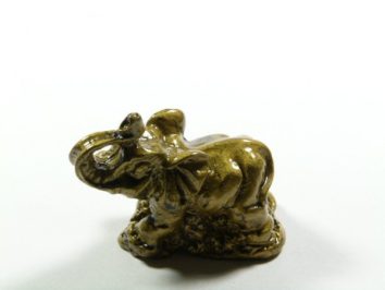 Mała ceramiczna figurka słonia na białym tle, słoń stoi z uniesioną trąbą.