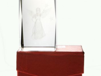 Szklana statuetka z wygrawerowanym aniołem stoi na czerwonym pudełku.