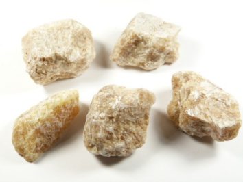 Kalcyt sunshine - kamień naturalny, surowy, nieszlifowany. Pięć kawałków surowego, jasnobrązowego minerału leży na białym tle.