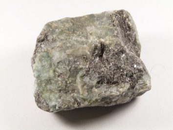 Szary, nieoszlifowany kamień minerału leżący na białym tle.