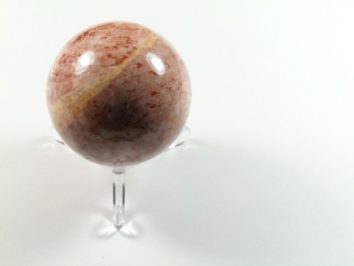 Kula z różowego kamienia na przezroczystym stojaku, ustawiona na białym tle.