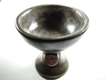 Ciemna, ceramiczna misa na nodze z wyrytym symbolem gwiazdy Dawida na podstawie.