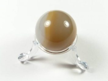 Kula karneol na podstawce. Kula z brązowego kamienia na przezroczystym stojaku, widok z góry, białe tło.