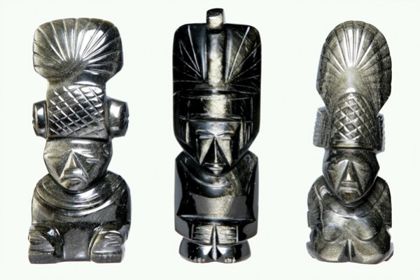 Trzy czarne figurki z kamienia przedstawiające postacie w ozdobnych nakryciach głowy.