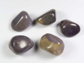 Waryscyt fioletowy - kamień gładzony, polerowany, szlifowany i bębnowany w formie otoczaka. Pięć gładkich, polerowanych kamieni o fioletowo-brązowej barwie na białym tle.