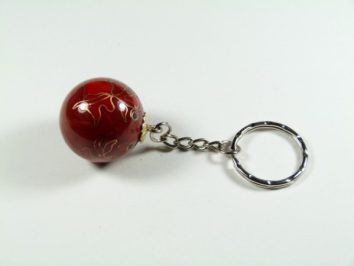 Breloczek z czerwonym, ozdobnym koralikiem na metalowym łańcuszku.