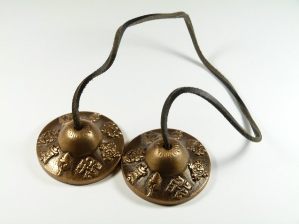 Dwie tybetańskie cymbałki tingsha połączone sznurkiem, leżą na białym tle.