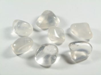 Siedem gładkich, przezroczystych kamieni leży na białej powierzchni.