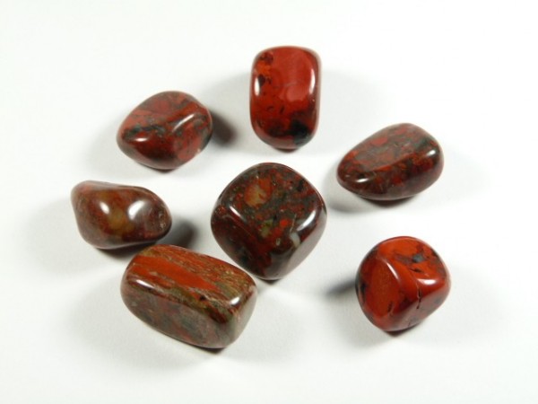 Jaspis brekcja - kamień gładzony, polerowany, szlifowany i bębnowany w formie otoczaka. Siedem polerowanych, czerwono-brązowych kamieni leży na białym tle.
