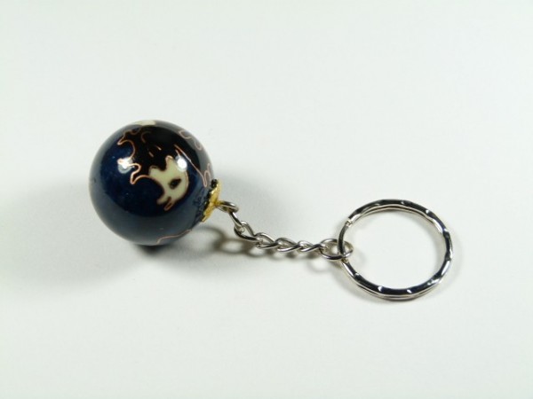 Breloczek z okrągłą, ciemną zawieszką ozdobioną wzorami, leży na białym tle.